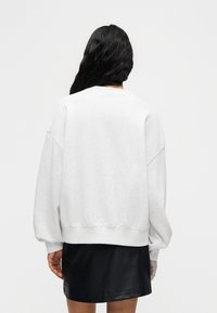 Φούτερ σε ανοιχτό γκρι βαμβακερό μείγμα, λαιμόκοψη crew, φαρδιά γραμμή, ωμοπλάτες που κατεβαίνουν, ριμπ μανσέτες και κάτω μέρος, συνδυασμένο με μαύρη μίνι δερμάτινη φούστα.