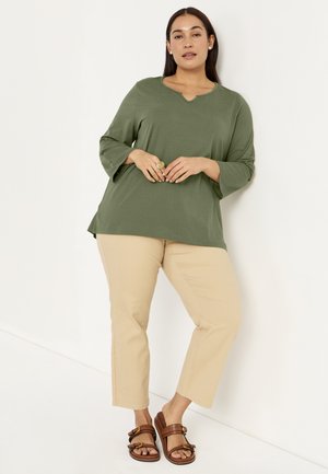 Olijf groene lange mouwen top met een V-hals, gecombineerd met beige cropped pantalons en bruine schuifsandalen met gespen. Glad textuur overal.
