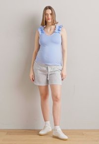 Débardeur bleu clair avec des bretelles volantées, associé à un short rayé gris et blanc, et des baskets blanches à finition texturée.