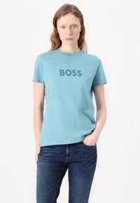Šviesiai mėlynas medvilninis marškinėliai su trumpomis rankovėmis ir apvaliu kaklu, su ryškiu tamsiai mėlynu "BOSS" logotipu priekyje.