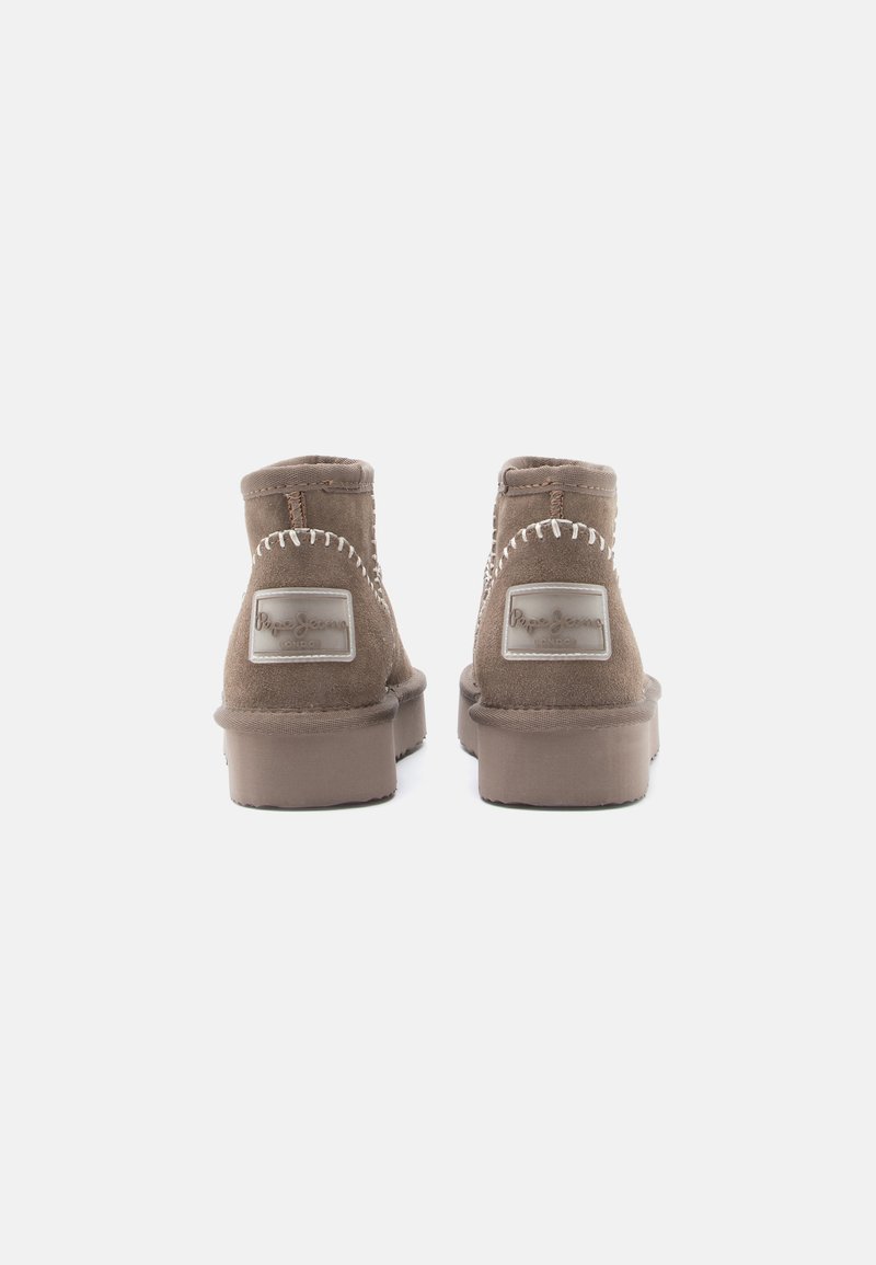 Braune Wildleder-Stiefeletten mit einer flachen Gummisohle, gesteppten Details und einem Logopatch. Die Rückansicht zeigt den umschlagenen Kragen und verstärkten Nähte.