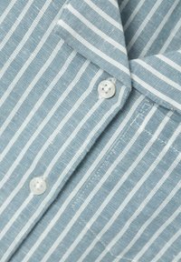 Camicia di stoffa a righe blu chiaro e bianche con colletto, caratterizzata da due bottoni perlacei e una texture morbida. Vista ravvicinata che evidenzia i dettagli.