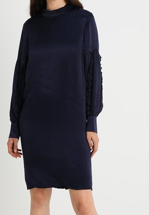Marineblauwe jurk met een hoge halslijn, lange, gerimpelde mouwen en een losse pasvorm. De stof heeft een subtiele textuur en een lichte glans.