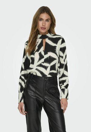 Top lungo a maniche lunghe con motivo bianco e nero e scollatura a chiave, abbinato a pantaloni in pelle nera a vita alta con tasche frontali.