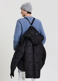 Giacca a vento nera con design trapuntato, indossata sulla schiena di un uomo. Si notano anche un berretto grigio e un maglione blu con trama.