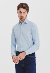 Jasnoniebieska koszula z długim rękawem, wykonana z gładkiego materiału, z kołnierzykiem w kształcie szpilki, w połączeniu z ciemnoniebieskimi dżinsami.