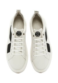 Baskets en cuir blanc avec des accents noirs, lacets plats et un badge rond "ÉDITION LIMITÉE" sur la languette. Texture lisse et bout arrondi.