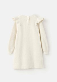 Pleťově krémové pletené šaty s dlouhými rukávy, volánkovými zdobením na ramenou a třemi knoflíky na zadním výstřihu. Měkká textura.