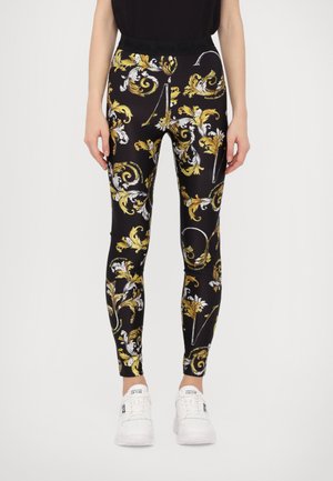 Leggings negras con un elaborado patr�ón floral en blanco y amarillo, con un diseño ajustado y una cinturilla elástica. Combinadas con zapatillas blancas.