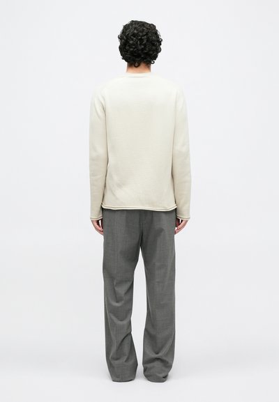 Ανοιχτό μπεζ πουλόβερ με στρογγυλή λαιμόκοψη, κατασκευασμένο από απαλό ύφασμα, συνδυασμένο με γκρι, φαρδιά παντελόνια με διακριτικό σχέδιο.