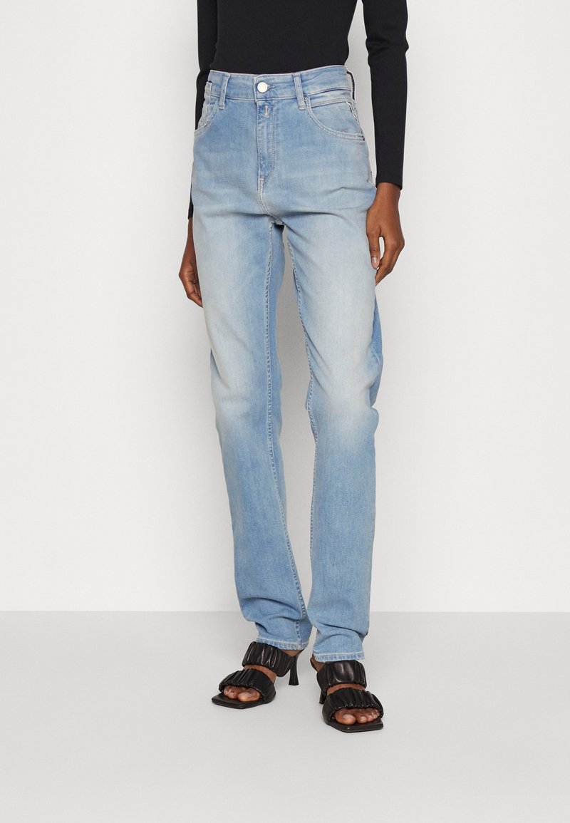 Ljust blå denimjeans med hög midja, rak benmodell och femfickorsdesign; kombinerat med svarta sandaletter med klossheel.