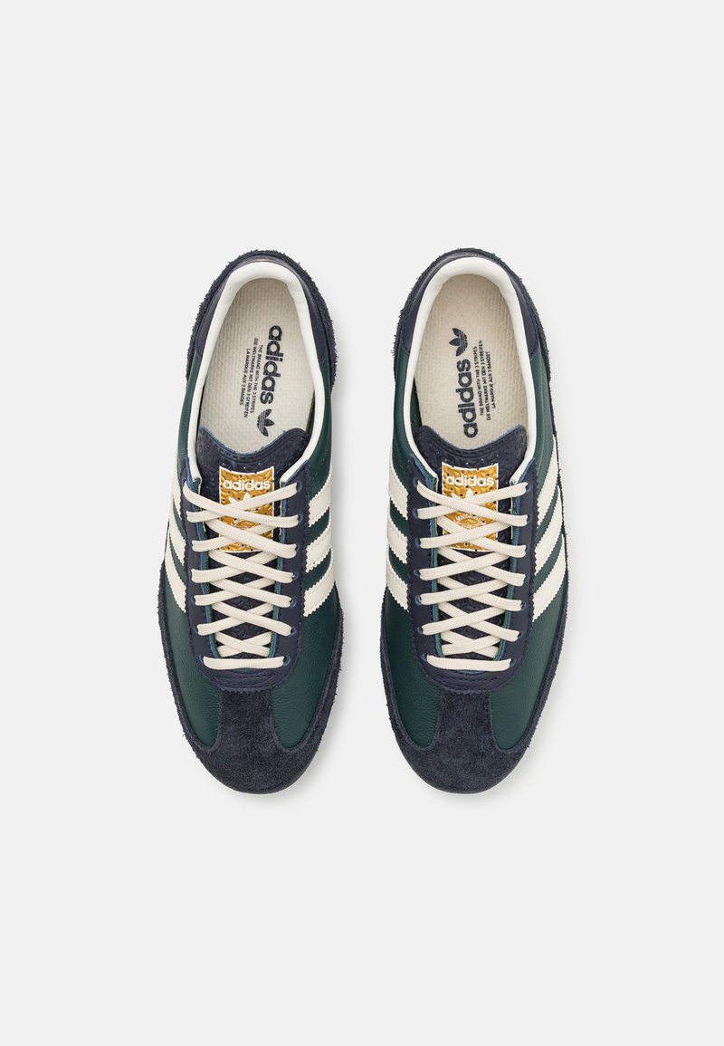 Zapatillas verdes y marino con rayas blancas, de material de gamuza y cuero, con cordones planos y detalles dorados en la lengüeta. Suela texturizada.