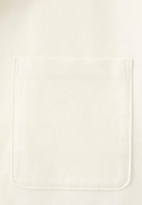 Tela blanca con una textura suave que presenta un bolsillo parche, forma rectangular y detalles de costura sutiles alrededor de los bordes.