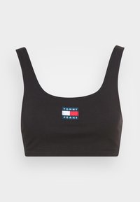 Svart croppad linne med breda band, tillverkad av mjukt tyg. Har en rektangulär logotyp i blått, rött och vitt. Slät yta.