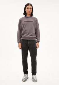 Grauener Kapuzenpullover mit "ARMEDANGELS" Druck, kombiniert mit schwarzen Jeans und silbernen Sportschuhen. Der Stoff hat eine glatte Textur und eine lockere Passform.