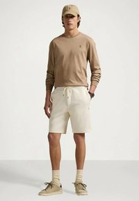 Beige μακρυμάνικο πουκάμισο, κρεμ σορτς, μπεζ αθλητικά παπούτσια και καπέλο ταύτισης. Μαλακά υλικά, σορτς με κορδόνι, απλός σχεδιασμός με λογότυπα.