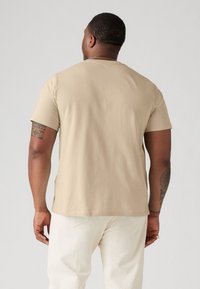Beige, rövid ujjú póló sima anyagból, laza szabással. Finom varrási részletekkel és kerek nyakkivágással rendelkezik.