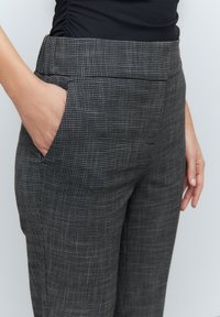 Pantaloni grigi a scacchi realizzati in un tessuto intrecciato; presentano tasche frontali e una vestibilità sartoriale. La texture è liscia con un motivo sottile.