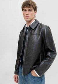 Schwarze Lederjacke mit Kragen, vorderem Reißverschluss und zwei Seitentaschen. Trägt man über einem weißen Hemd und blauen Jeans. Glatte Textur.