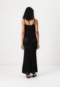 Μαύρο μέγιστο φόρεμα με βελονάκι, λεπτές τιρά�ντες και εφαρμοστή σιλουέτα. Το ύφασμα έχει ανοιχτό πλεκτό σχέδιο με γεωμετρικά μοτίβα.