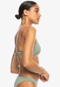 Zelený bikiny set vyrobený z hladkého materiálu; trojuholníkový vrch s prekríženými popruhmi, viazaný na chrbte, doplnený o nohavičky s nízkym pásom.
