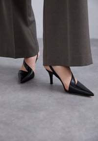 Escarpins noirs en cuir avec une pointe fine et des talons fins. Ils présentent un design de sangle architectural et une finition lisse.