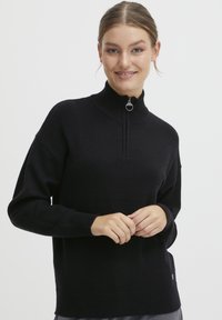 Črn pulover s visokim ovratnikom in pol-zadrgo. Mehka tekstura, sproščen kroj ter rebrasti manšeti in rob. Diskreten logotip.