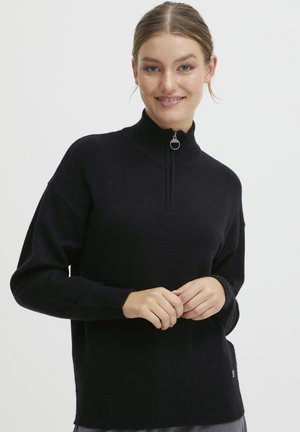 Maglione nero a collo alto con zip a metà. Tessuto morbido, vestibilità rilassata e polsini e orlo a coste. Dettaglio del logo discreto.