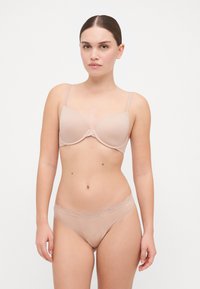 Ensemble de lingerie couleur chair composé d'un soutien-gorge lisse et rembourré et de briefs hipster assortis avec une dentelle sur la taille. Tissu doux et élastique.