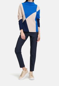 Pull en tricot avec motifs géométriques beiges et bleus, associé à un pantalon marine et des baskets beiges à semelles blanches.