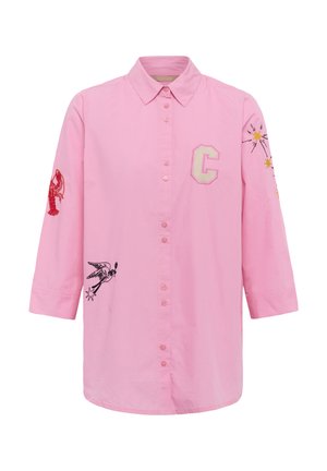 Chemise rose à manches longues avec boutons, brodée d'une lettre C, d'un homard rouge sur la manche gauche, d'un oiseau noir sur le devant et d'étoiles jaunes sur la manche droite.
