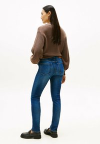 Pull en maille marron avec des manches volumineuses, associé à un jean en denim bleu ajusté. L'ensemble est complété par des mocassins noirs.