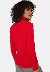 Pull à col montant rouge avec texture côtelée, design ajusté, manches longues et encolure haute. Ourlet lisse au niveau de la taille.