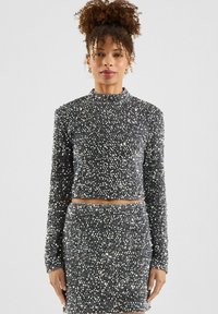 Silberner, mit Pailletten besetzter Cropped-Pullover mit langen Ärmeln, kombiniert mit einem passenden, hochgeschnittenen Rock. Glatte Textur mit reflektierenden Elementen.