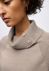 Ljusgrå tröja med en texturerad, vikbar krage och två grå knappar. Har ribbade detaljer på axlarna. Mjuk tyg.