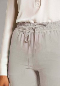 Lichtgrijze joggers van stof met een elastische tailleband en verstelbaar trekkoord. Glad textuur met een subtiele glans en een ontspannen pasvorm.