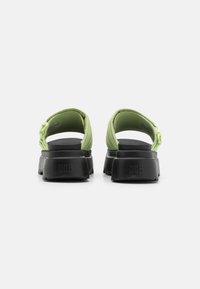 Sandalias de goma verdes con una suela gruesa negra, que cuentan con una correa trasera y un logotipo de UGG destacado en el talón. Textura suave y diseño simple.