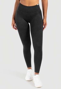 Schwarze hoch taillierte Leggings mit glatter Textur und figurbetontem Design, kombiniert mit weißen Sportschuhen.