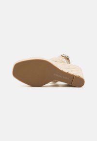 Beige kile sandal med vævet tekstur, justerbar ankelrem og gummisål med et mønstret dæk. Let hæl hævning.