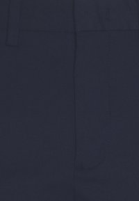 Marinblå tygbyxor visar en fin texturerad väv, med en enda sidficka och skräddarsydda sömmar. Slät yta utan synliga mönster.