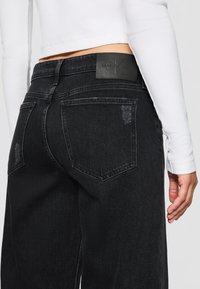 Black denim jeans with a straight cut, featuring a distressed look and back pockets. A Calvin Klein logo patch is visible on the waistband.