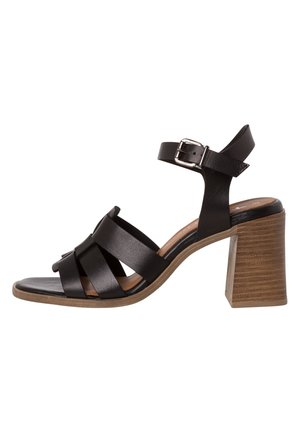 Black leather heeled sandal with an ankle strap, cross straps over the toe, and a chunky wooden heel. Smooth texture with a flat sole.