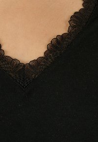 Zwarte top met een V-hals en ingewikkelde zwarte kanten rand langs de halslijn. De stof lijkt zacht met een lichte textuur.