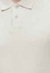 Polo beige avec deux boutons et texte de logo en relief « BOSS » sur la poitrine gauche.