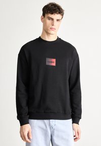 Μαύρο φούτερ με λαιμόκοψη crew, που φέρει ένα ορθογώνιο λογότυπο σε κόκκινο και μαύρο. Κομμένο σε άνετη γραμμή με ριμπ μανσέτες και τελείωμα.