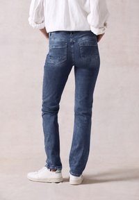Jeans ajustados azul oscuro con una textura de denim suave, con dos bolsillos traseros y una cintura de altura media, combinados con zapatillas blancas.