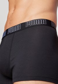 Schwarze Boxershorts aus glattem, dehnbarem Stoff mit breitem elastischem Bund, der das weiße "PUMA"-Logo trägt.