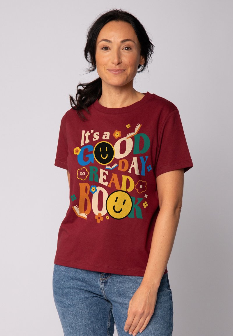 T-shirt en coton bordeaux avec un graphique coloré incluant le texte "C'est une BONNE journée pour LIRE un LIVRE", des visages souriants et des accents floraux.