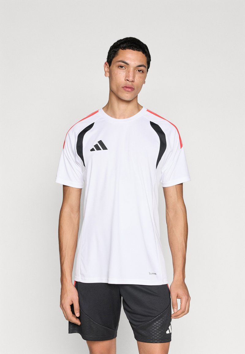 Λευκό αθλητικό t-shirt με μαύρες και κόκκινες λεπτομέρειες, κοντά μανίκια και μαύρο λογότυπο στο στήθος. Φοράται με σκούρο σορτς που έχει σχεδιαστικό μοτίβο.