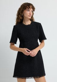 Mustissa lyhythihaisessa mekossa on teksturoitu kangas, jossa on liehuva helma ja kaula-aukko. Mekossa on istuva yläosa ja lievä A-linjainen muoto.